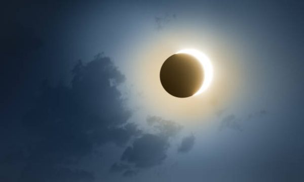 Solar Eclipse with dark blue sky and clouds.